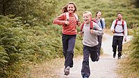 Eine Familie ist am Wandern und die zwei Kinder rennen auf dem Gehweg